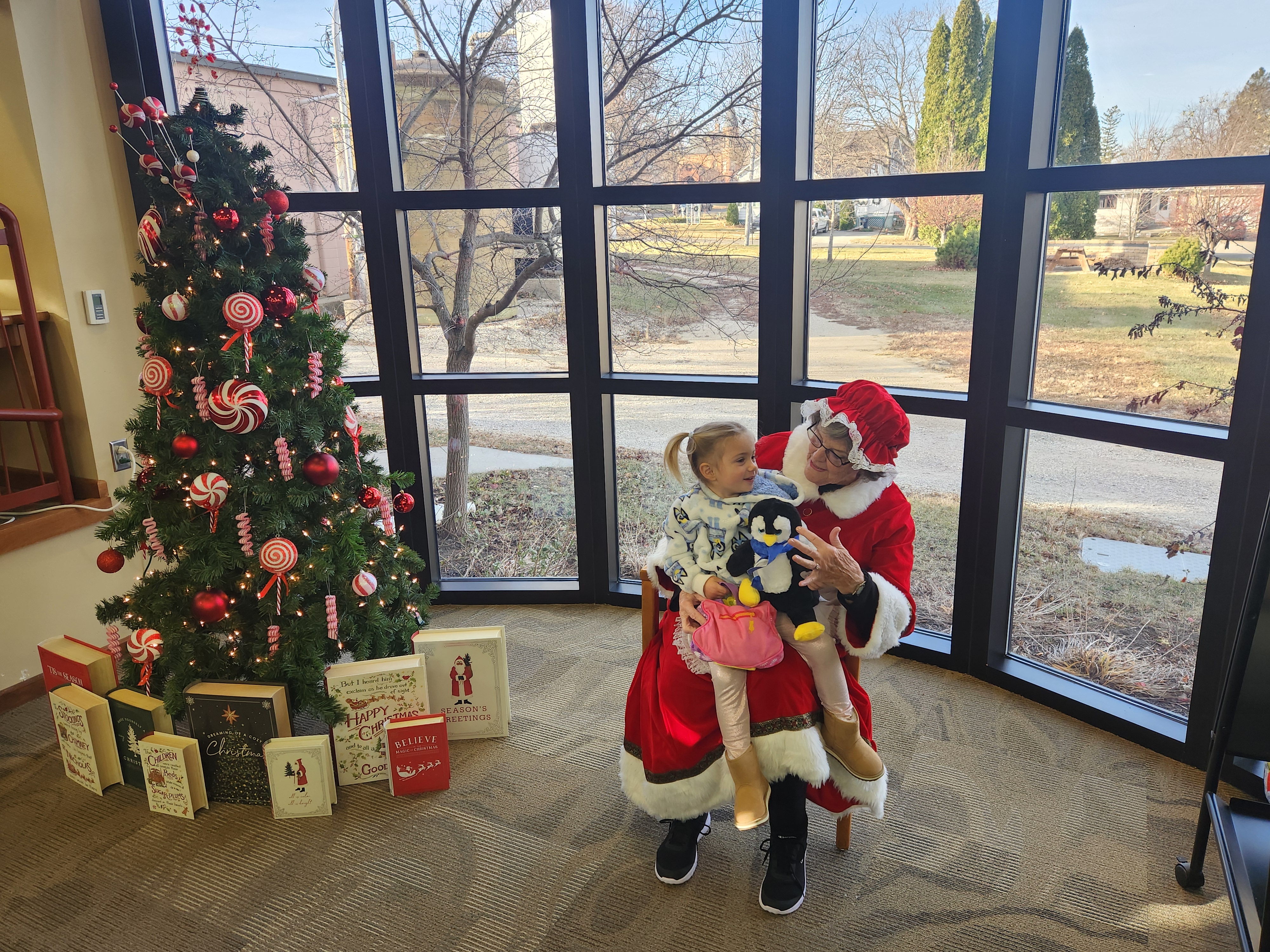 Friends Volunteer as Mrs. Claus with a child with their stuffed penguin a part of the Build a Bear Annual Event in December, partly sponsored by the Friends of the Library.